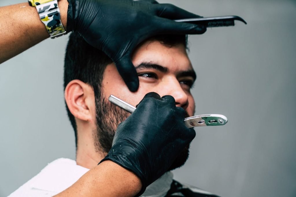 person-shaving-a-man-s-face-with-straight-razor-897251 Close-up of a barber shaving a mans beard with precision in a contemporary barbershop setting.